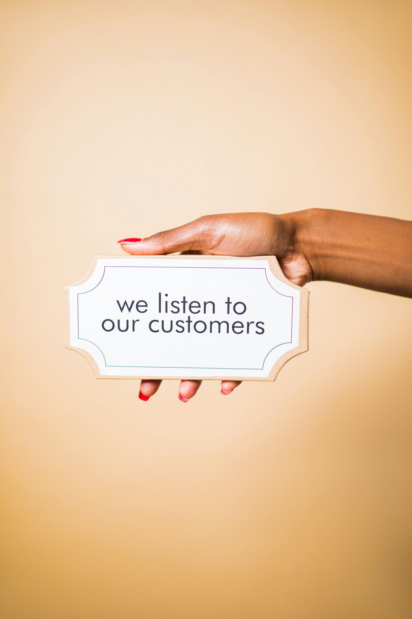 A hand holding a sign saying 'we listen to our customers' on a neutral background.